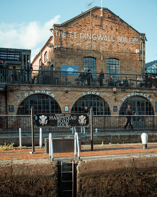 Exterior view of the historic Tedingwall Building, made of red brick with large arched windows and outdoor balcony railings, situated along the Camden Lock canal area. The balcony features a black met