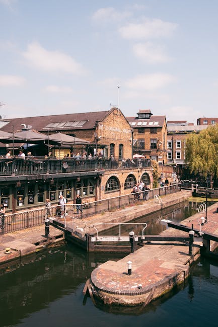 Exterior view of the historic Tedingwall Building, made of red brick with large arched windows and outdoor balcony railings, situated along the Camden Lock canal area. The balcony features a black met