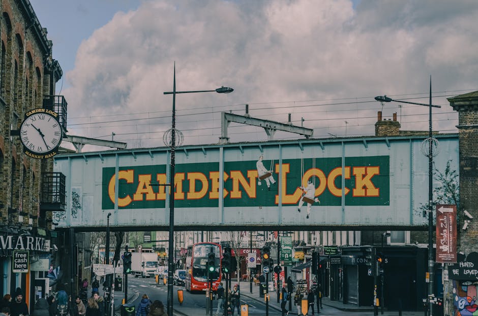 Three professional cleaners from Camden Cleaners are performing surface cleaning and deep cleaning in a modern living room. The room features a large, L-shaped fabric sofa positioned against a wall wi